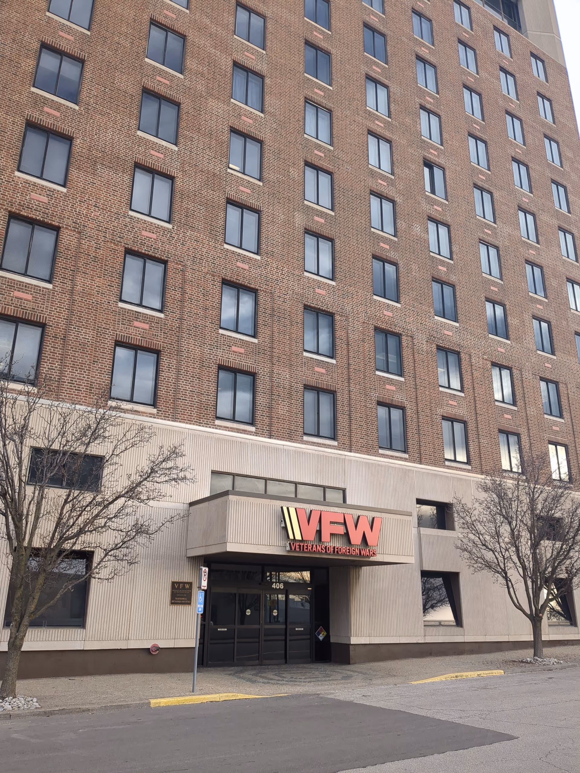 Tall brick building with an entrance and a red VFW sign at street level.
