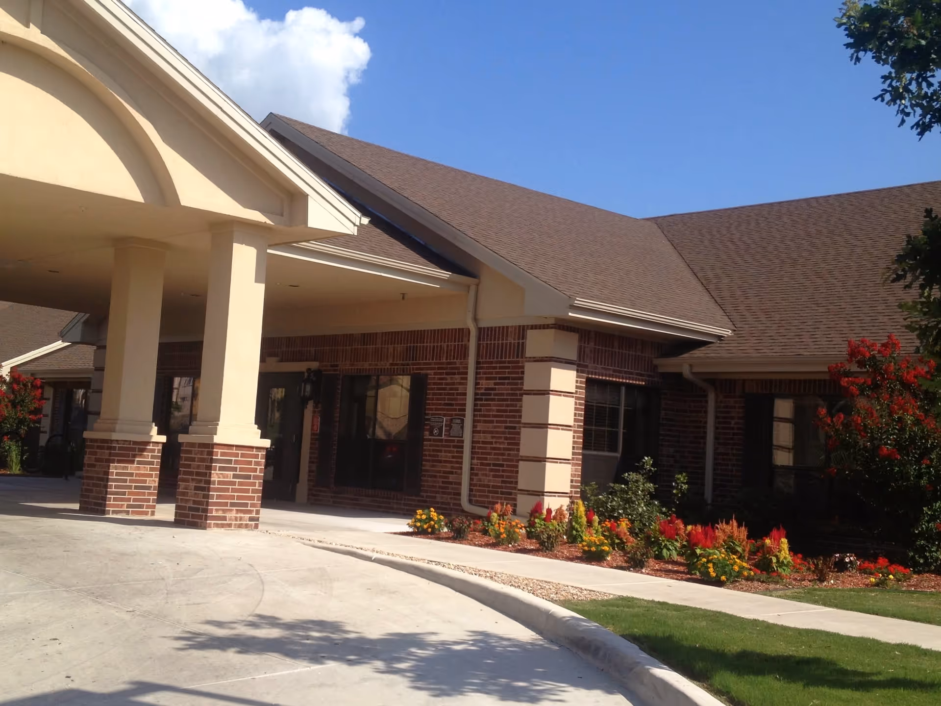 Exterior entrance of a senior living facility with brick walls, columns, and landscaped shrubs