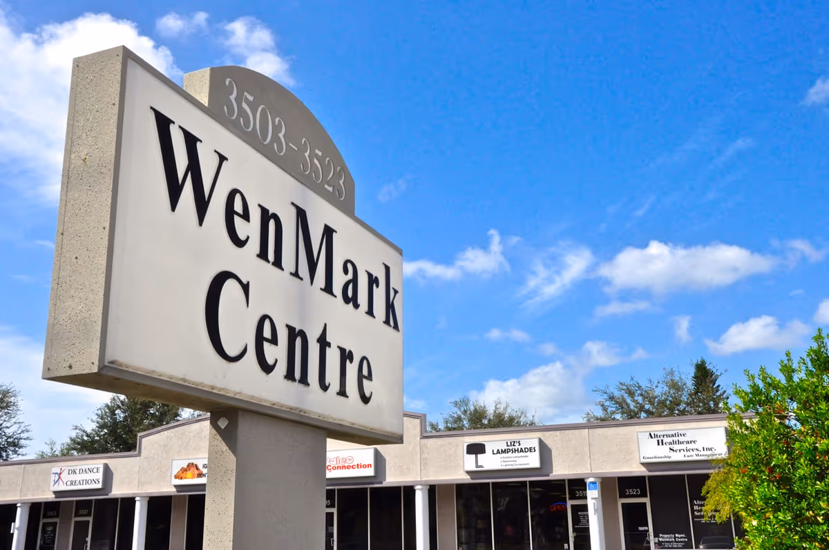 Front view of a strip mall with a WenMark Centre sign and storefronts.