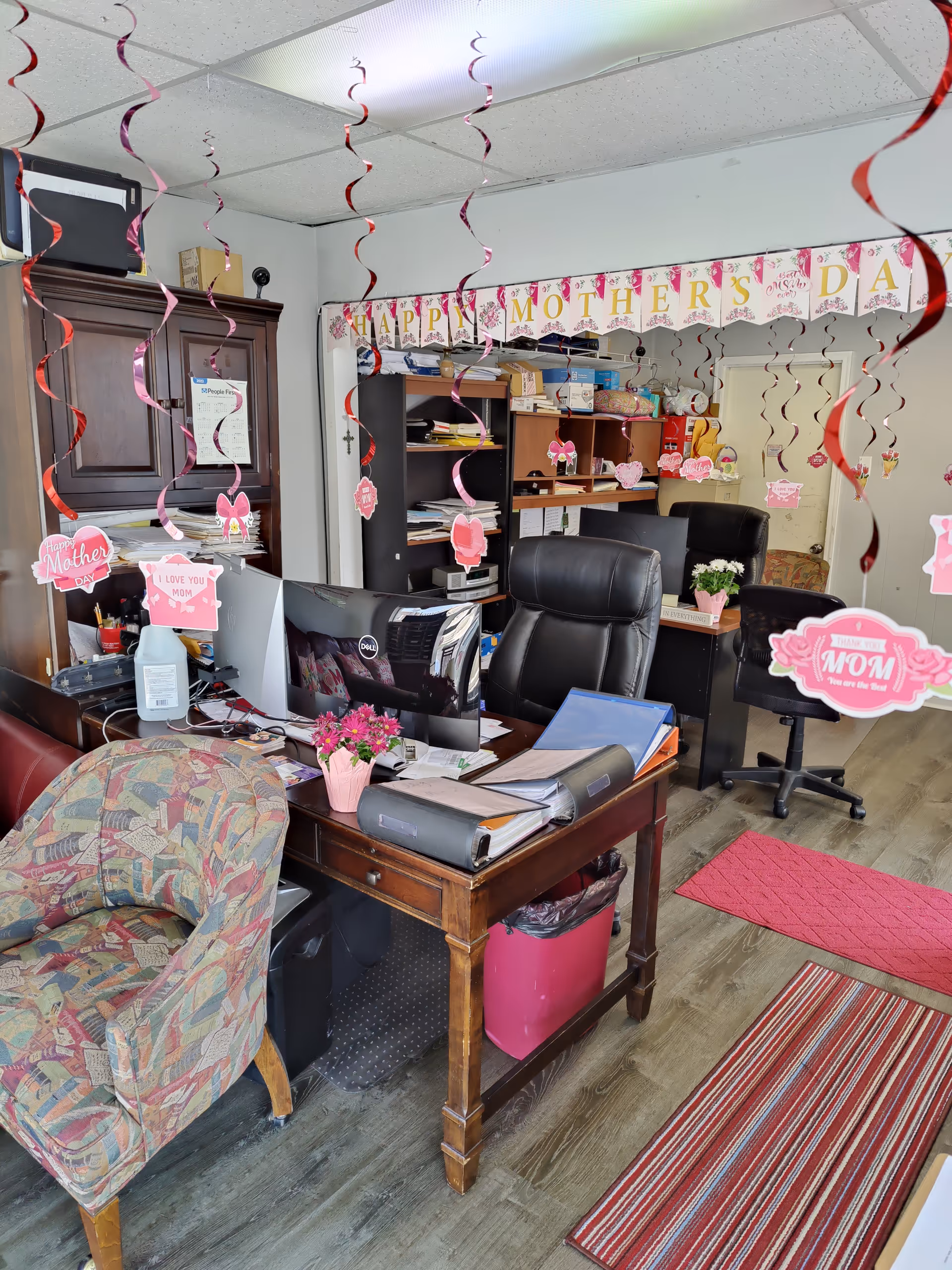 An office desk area with computers and pink Mother's Day decorations and streamers.