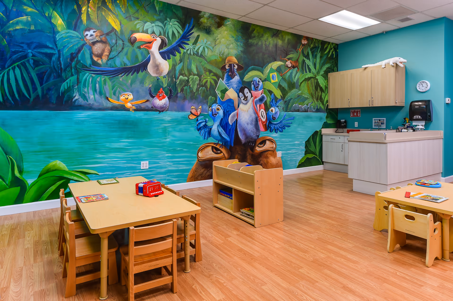 Colorful children's playroom with a mural, small tables, and a kitchenette.