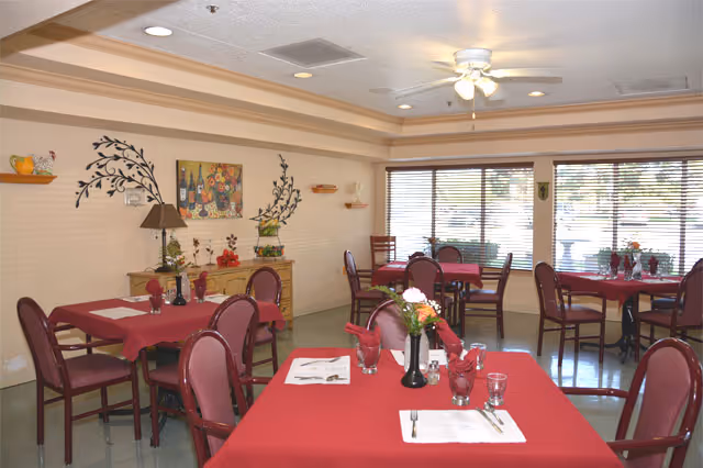 Bright dining room in a senior care center with red tablecloths and windows.