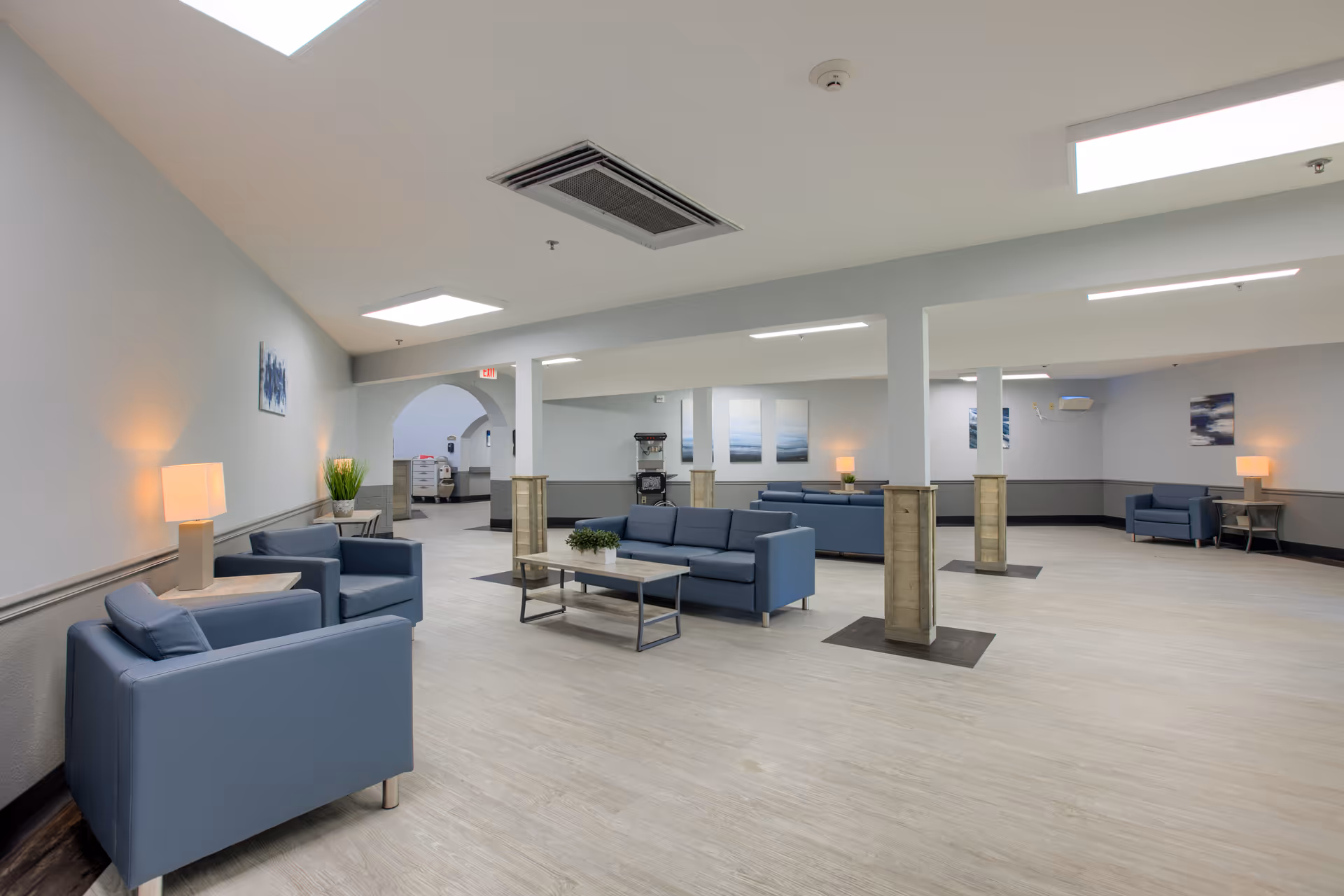Spacious senior living lounge with blue sofas, tables, and soft lighting.