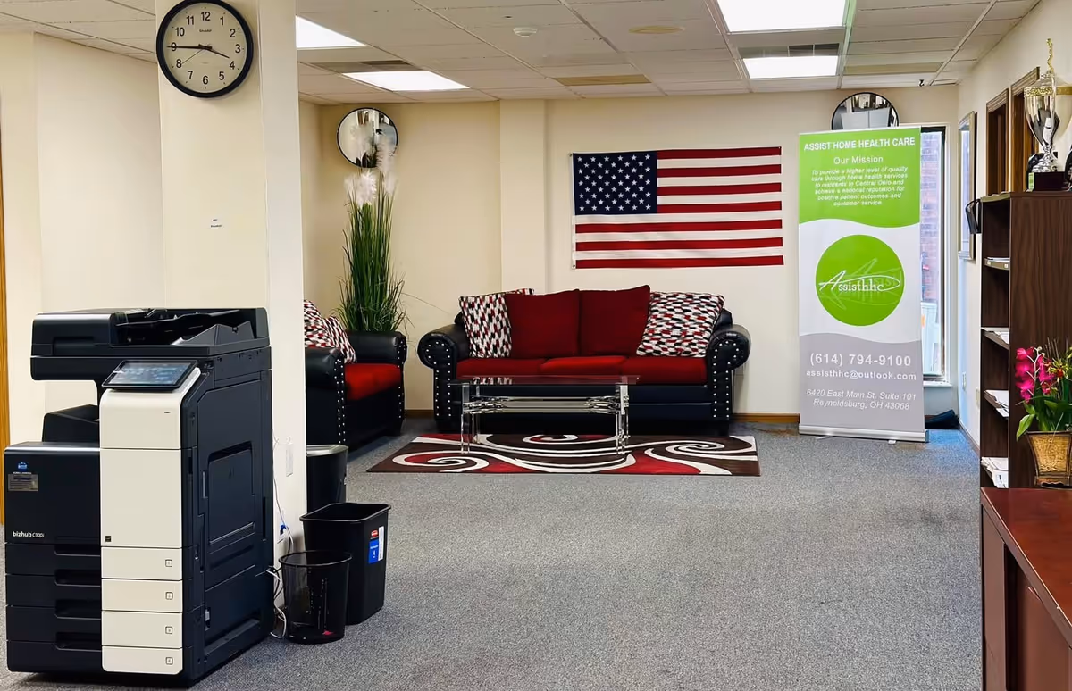 Lobby area with red sofa, American flag, banner, plants, and a copier.