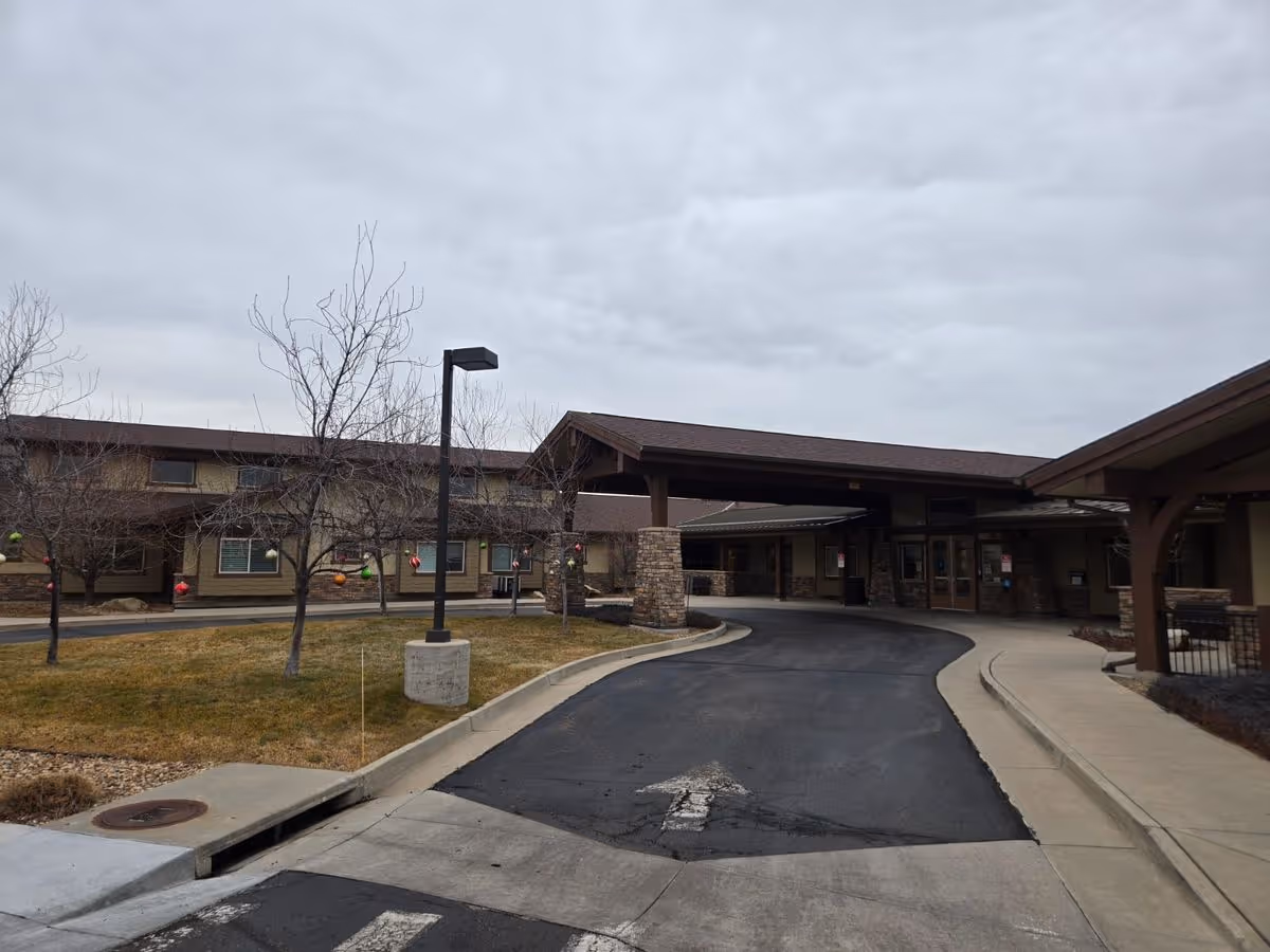 Driveway and covered main entrance of a single-story senior living building with leafless trees under an overcast sky.