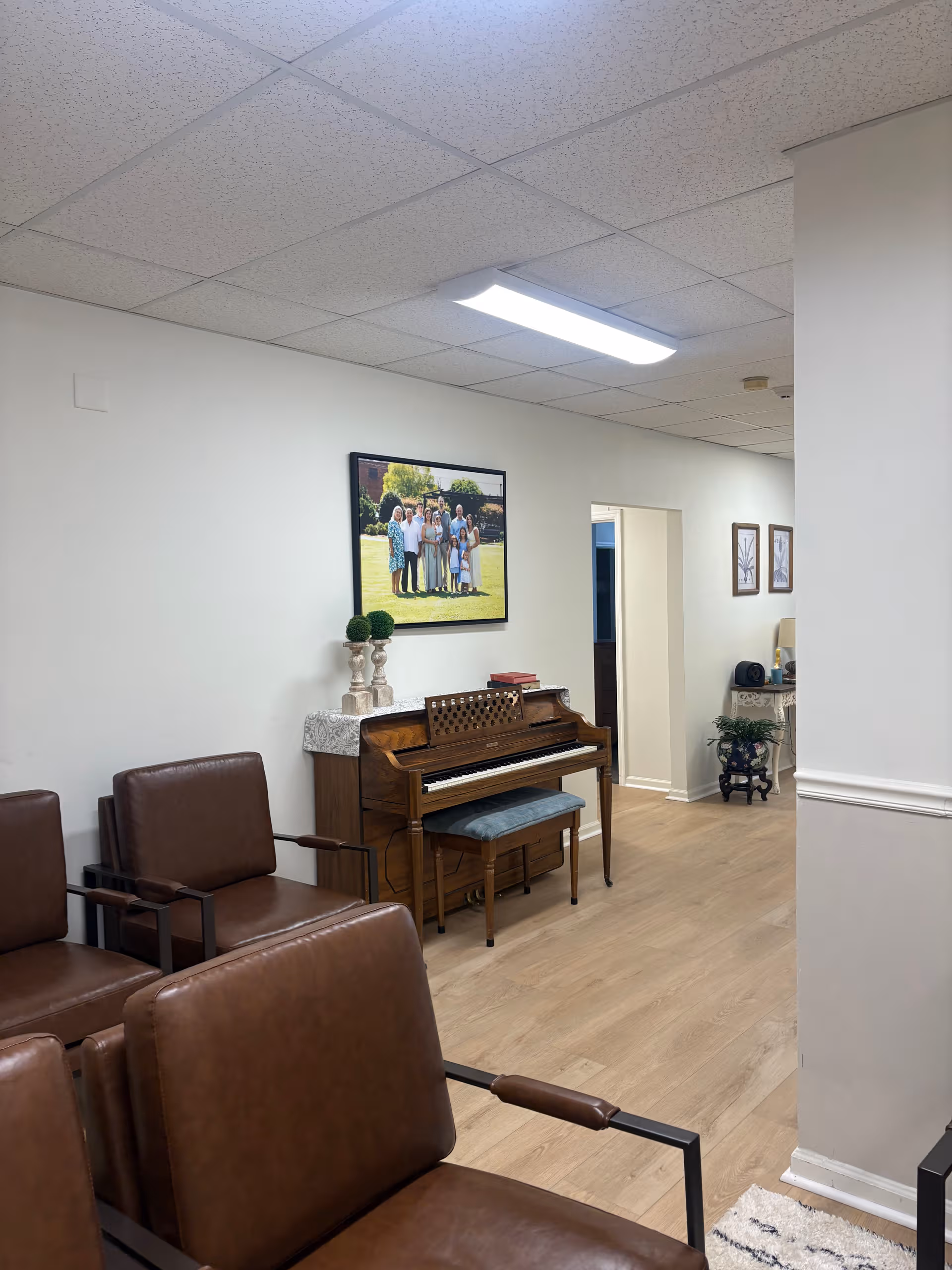 Interior common living area with brown leather chairs, a piano, and a framed photo on wall.