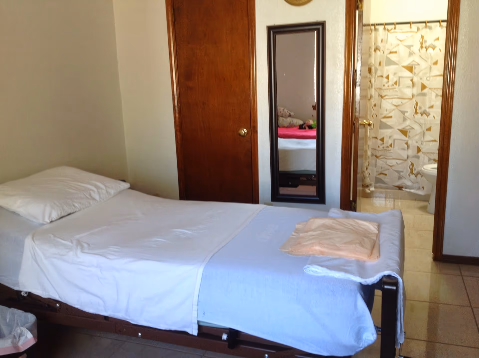 A bedroom with a bed, a full-length mirror, and a doorway to the bathroom.