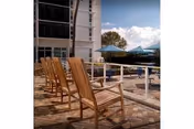 Row of wooden lounge chairs on a sunlit outdoor pool deck beside a building with umbrellas.