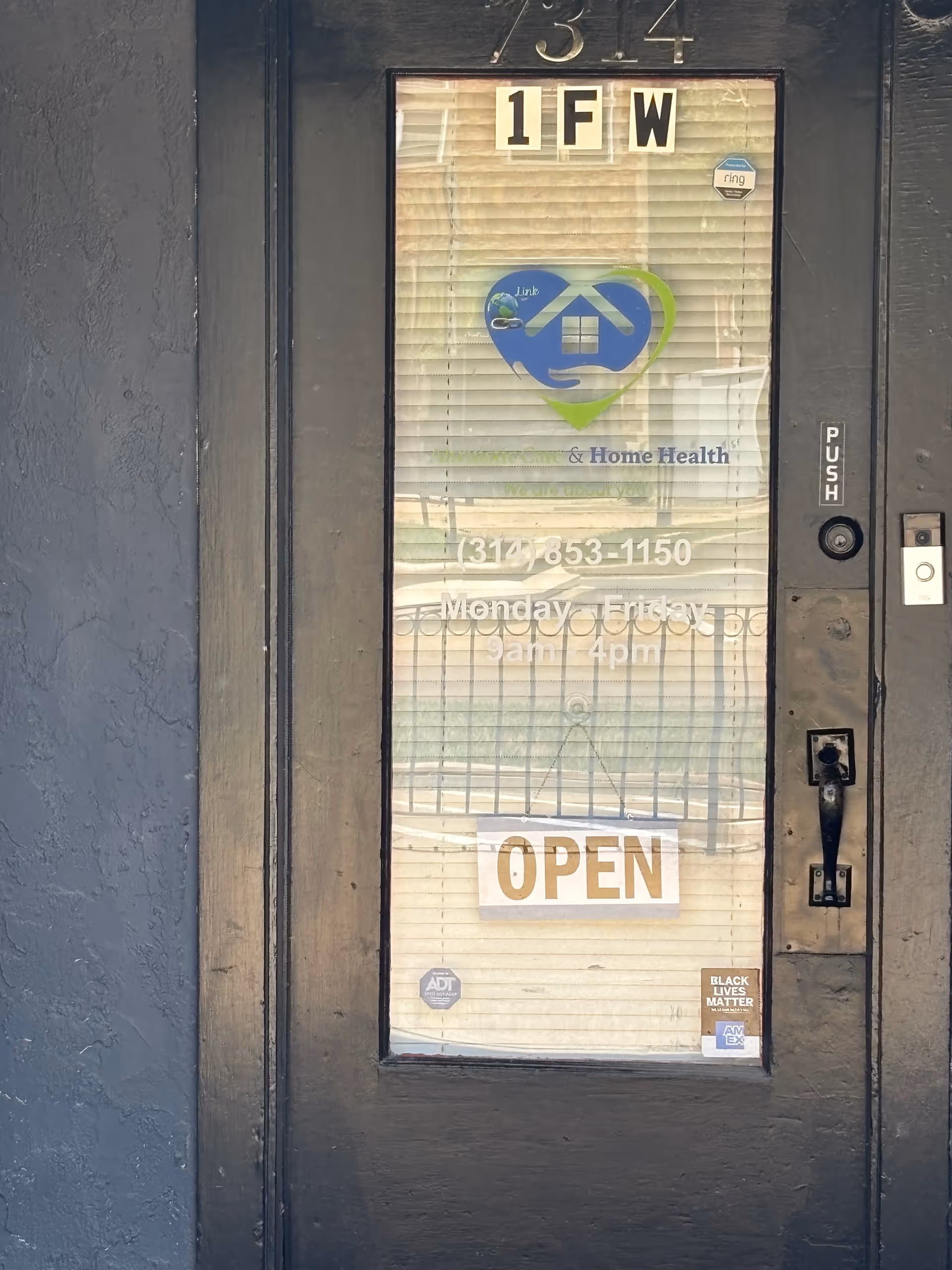 Front door of a care facility with blinds, signage, and an OPEN sign.