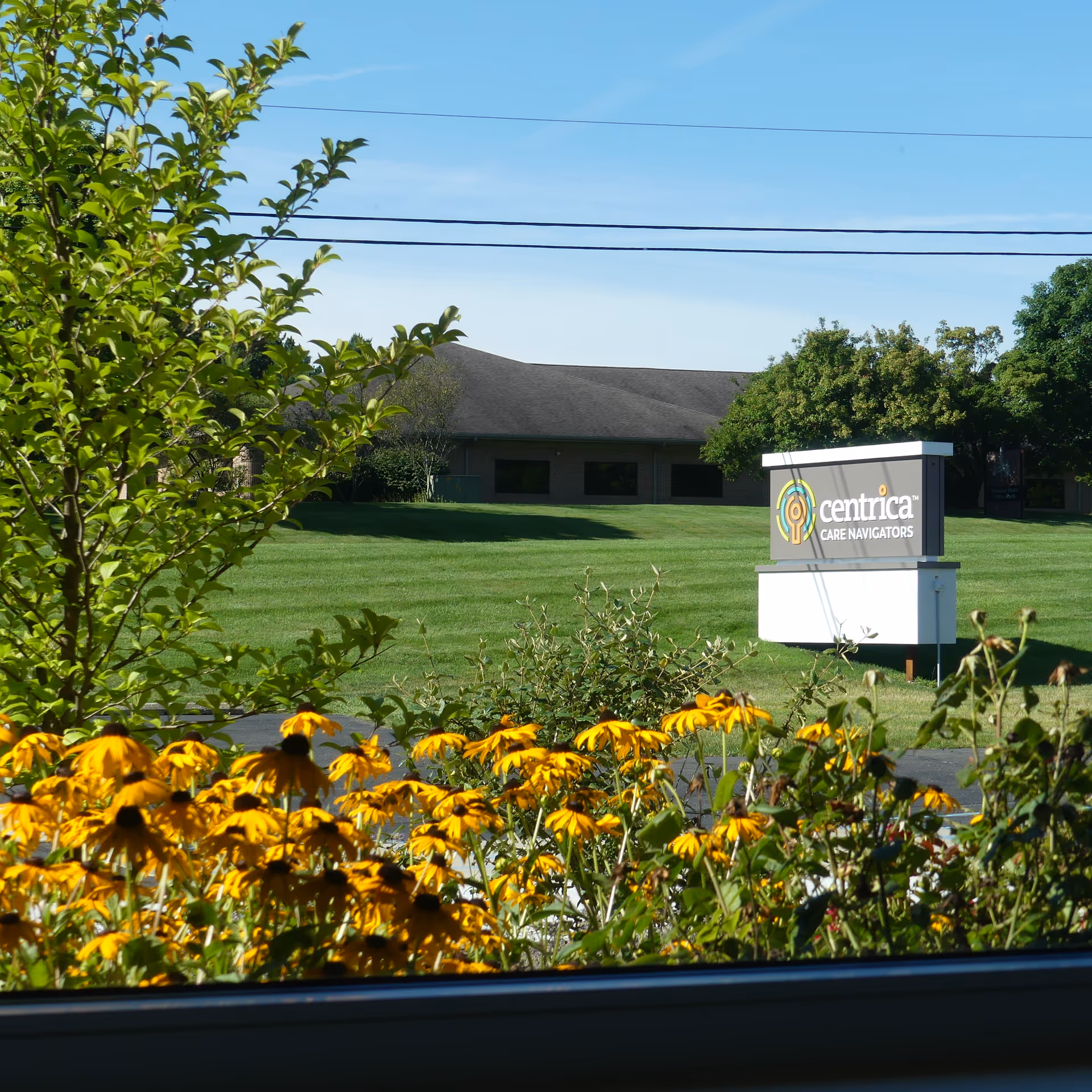 Exterior view of Centrica Care Navigators facility with sign, lawn, and yellow flowers.