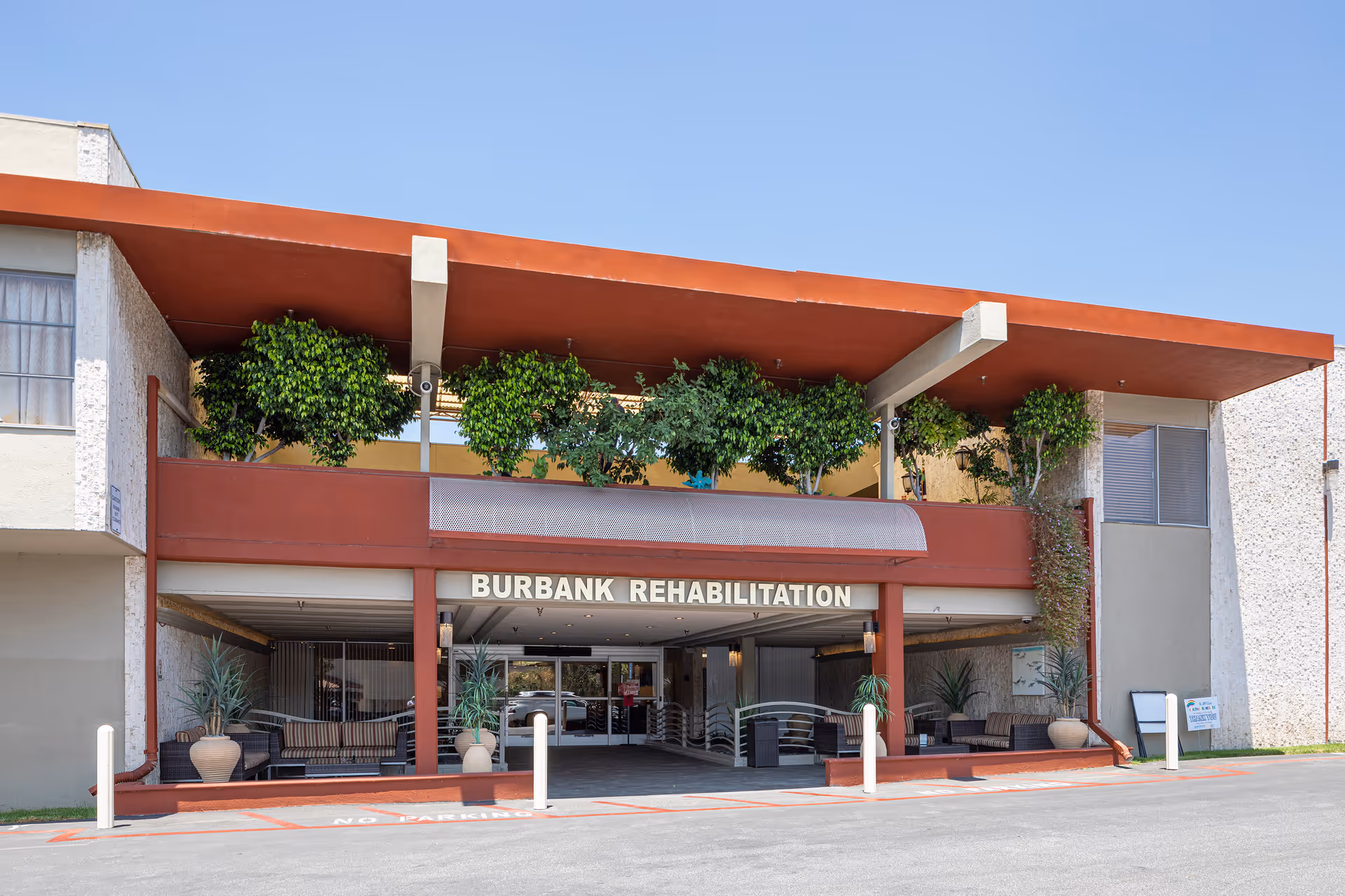 Exterior of Burbank Rehabilitation entrance with red canopy and greenery.