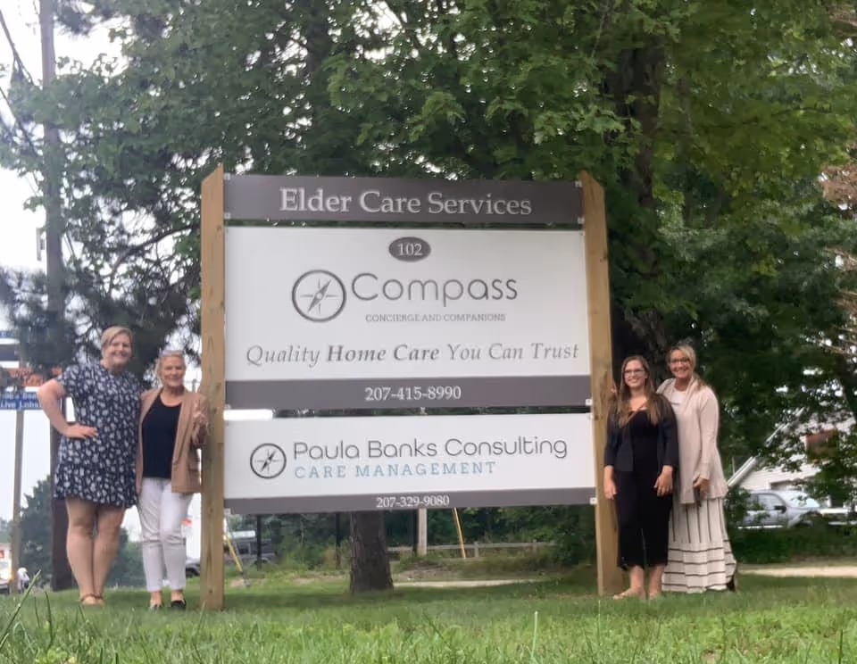Four people stand beside a large Compass sign outside an elder care facility.