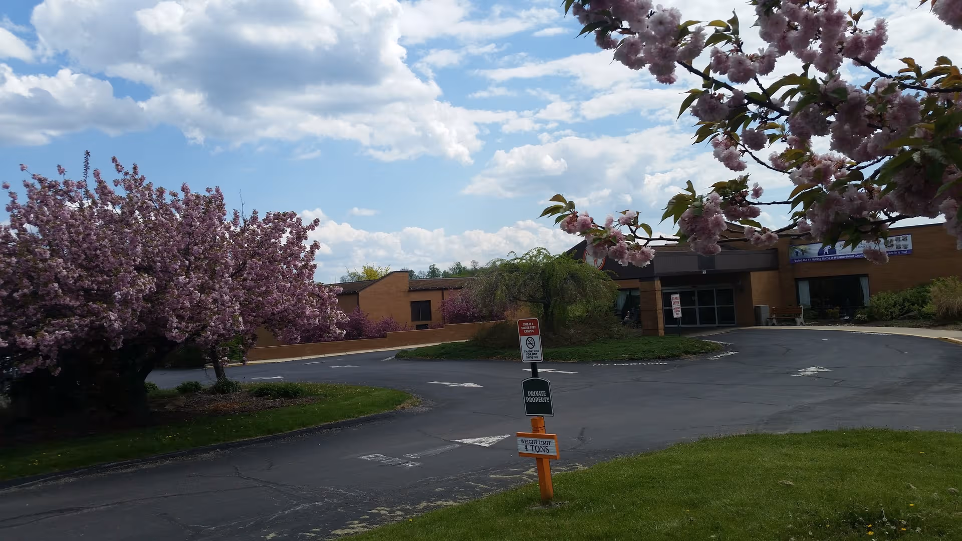 Exterior view of a brick senior living facility with flowering trees and a driveway