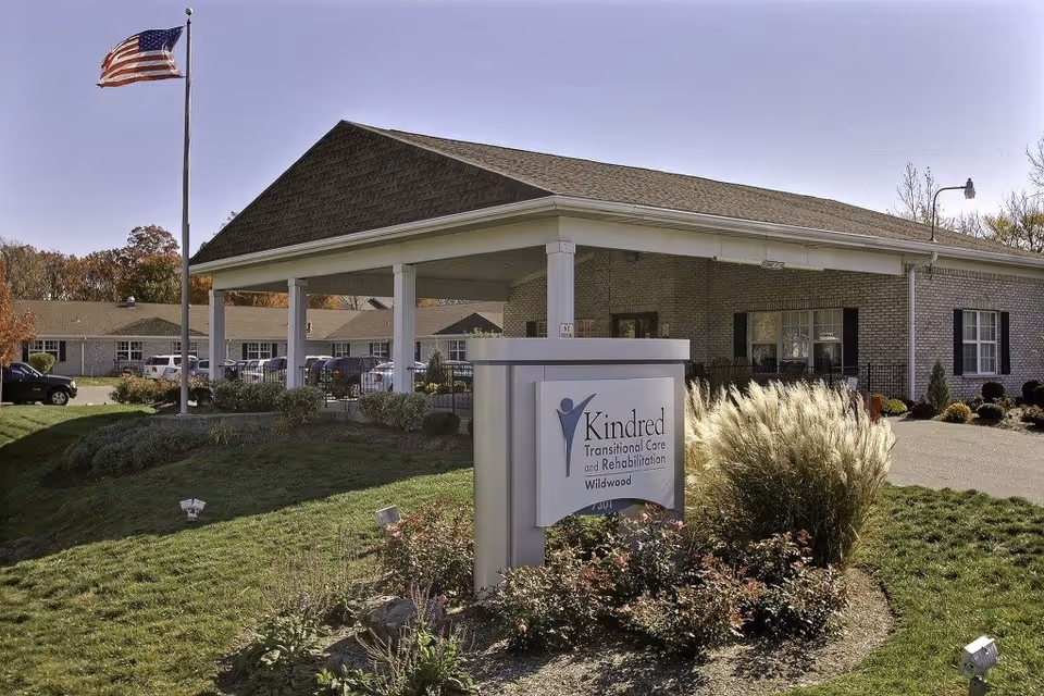 Exterior view of a senior care center with flag, sign, and covered entrance.