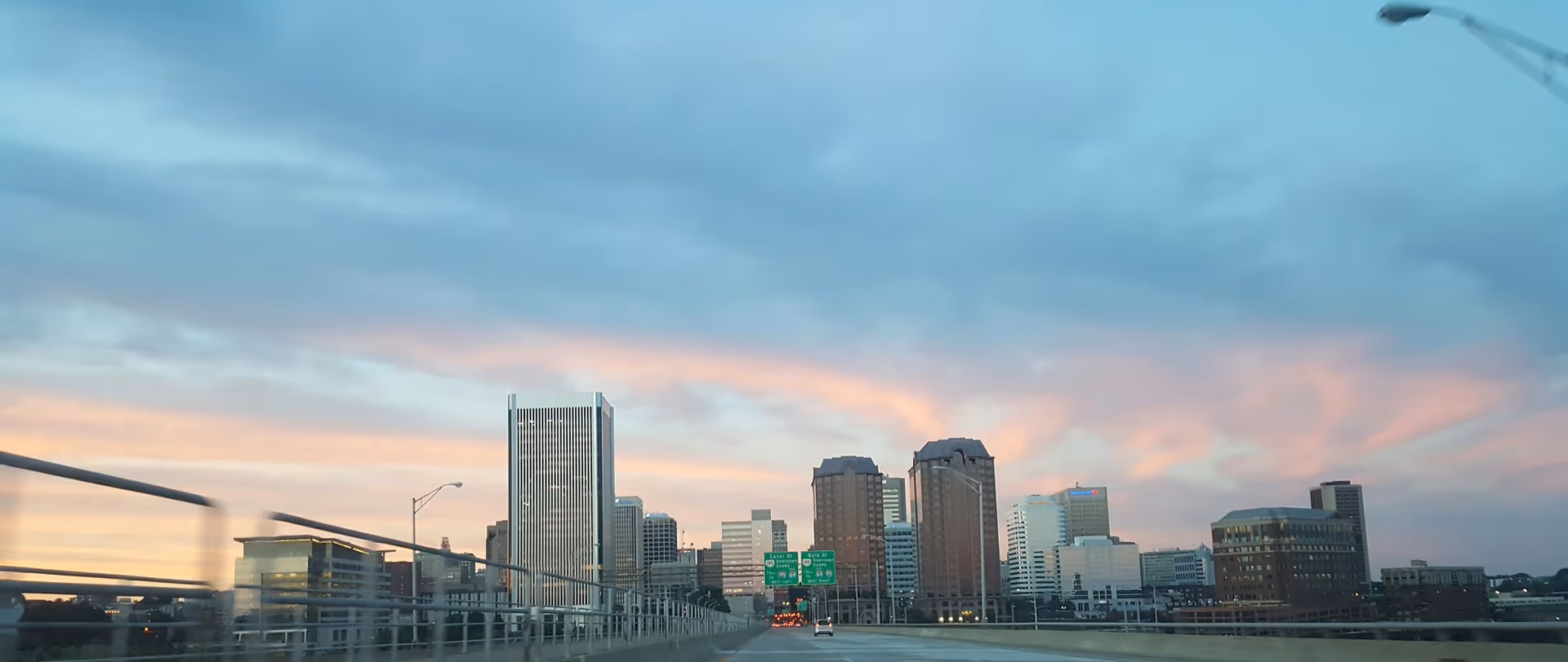 City skyline viewed from a highway overpass at sunset with railing