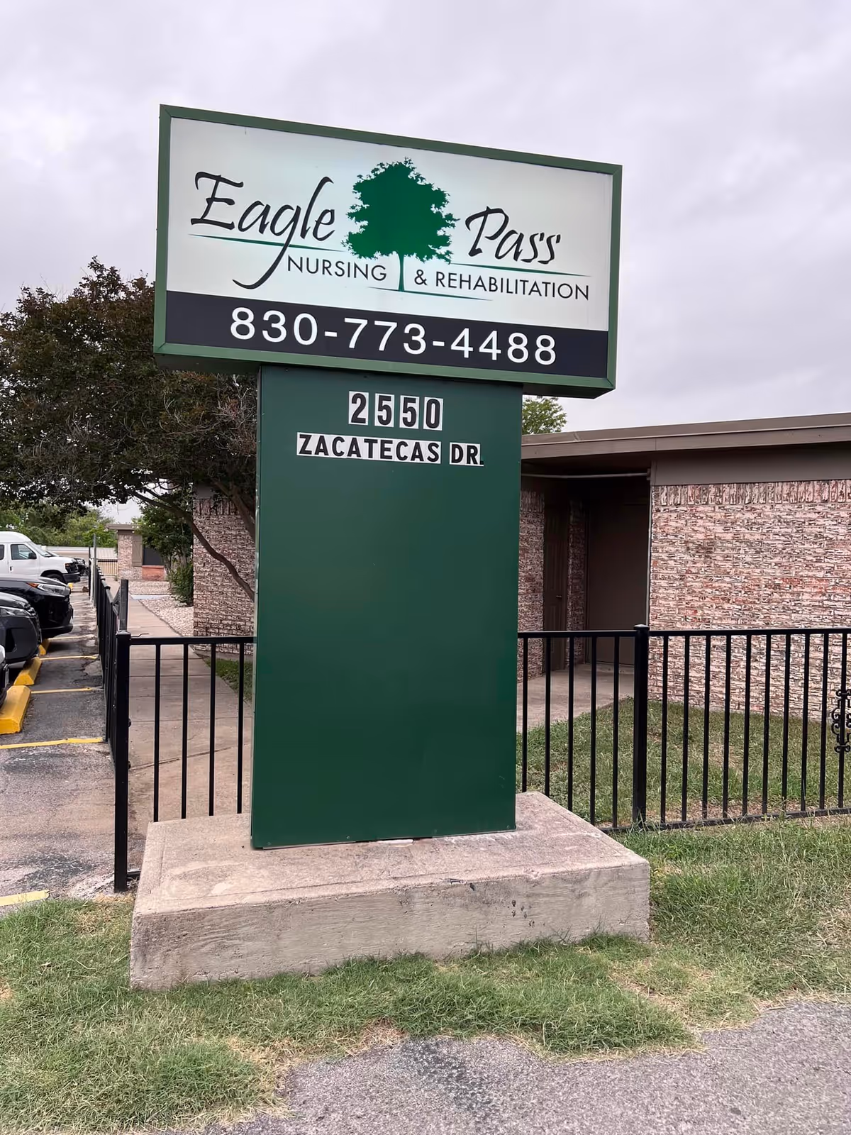 Outdoor sign for Eagle Pass Nursing & Rehabilitation with phone number 830-773-4488 and address 2550 Zacatecas Dr, situated on a concrete base with a building and parking lot in the background.