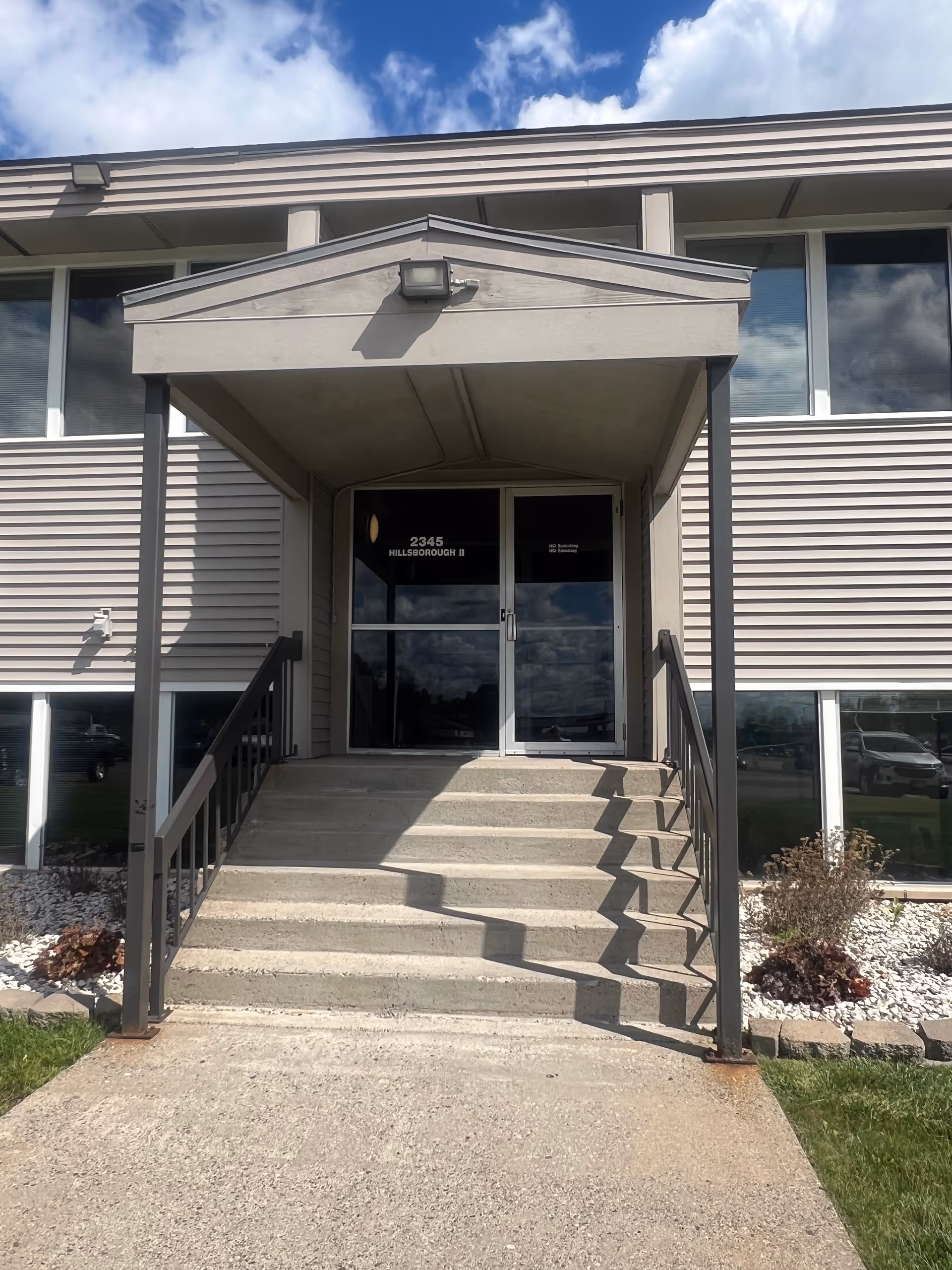 Exterior view of a senior living facility entrance with stairs and glass doors.