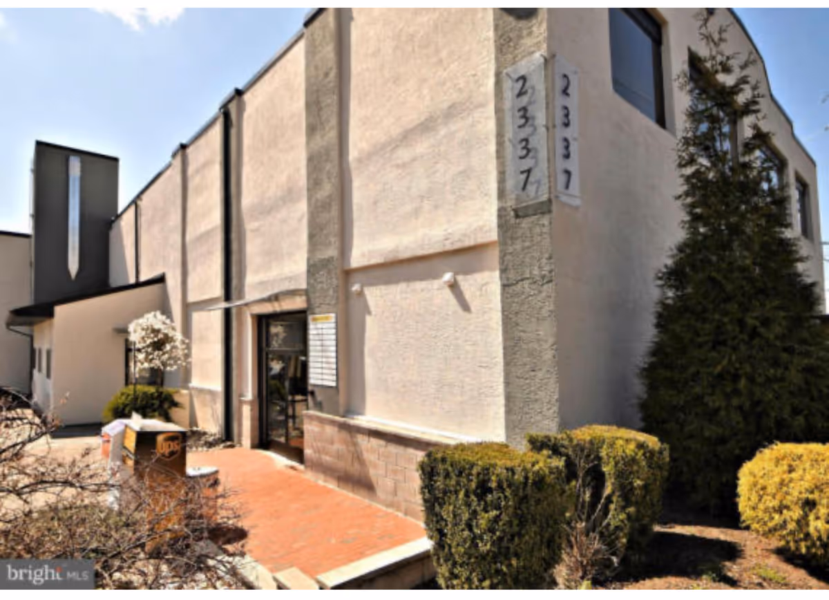 Beige exterior of a building with an entry door and landscaped shrubs.