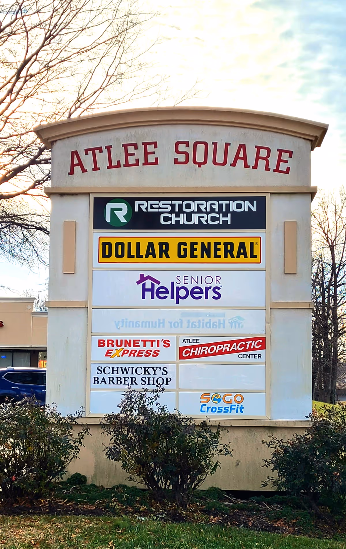Tall outdoor sign at Atlee Square listing businesses, including Senior Helpers and Dollar General.
