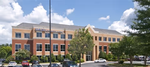 Front exterior of a brick medical building with landscaping and parked cars.