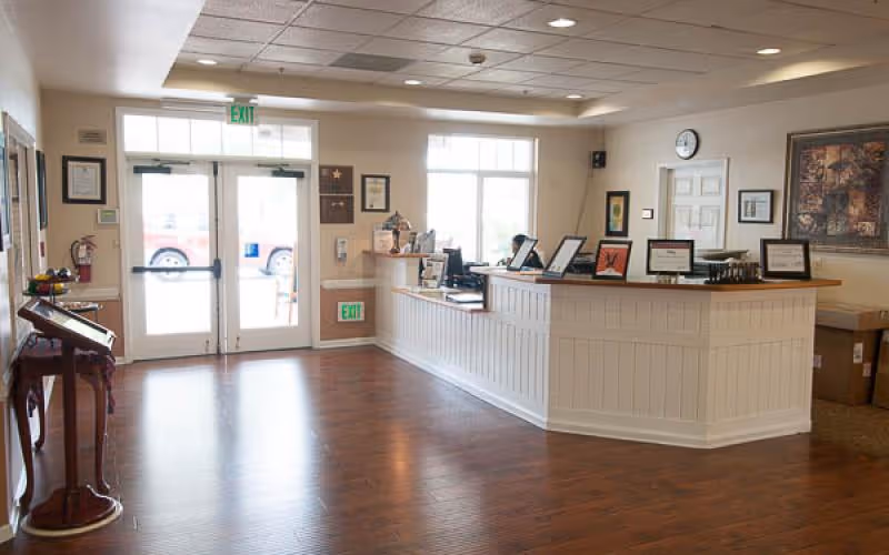 Interior lobby with a white paneled front desk, double doors, and wooden flooring.