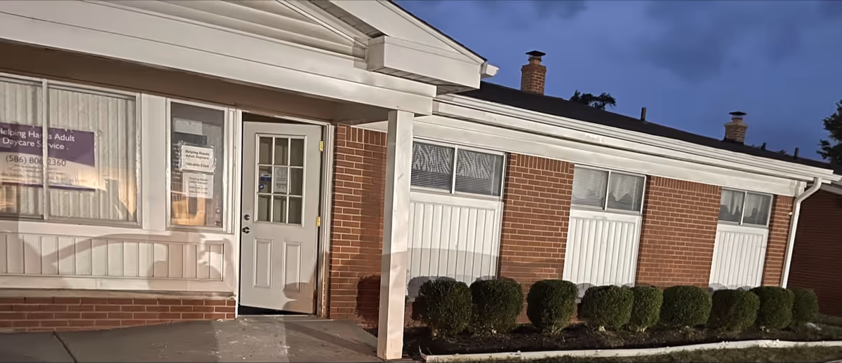Brick senior living facility exterior with a white entrance door and trimmed hedges.