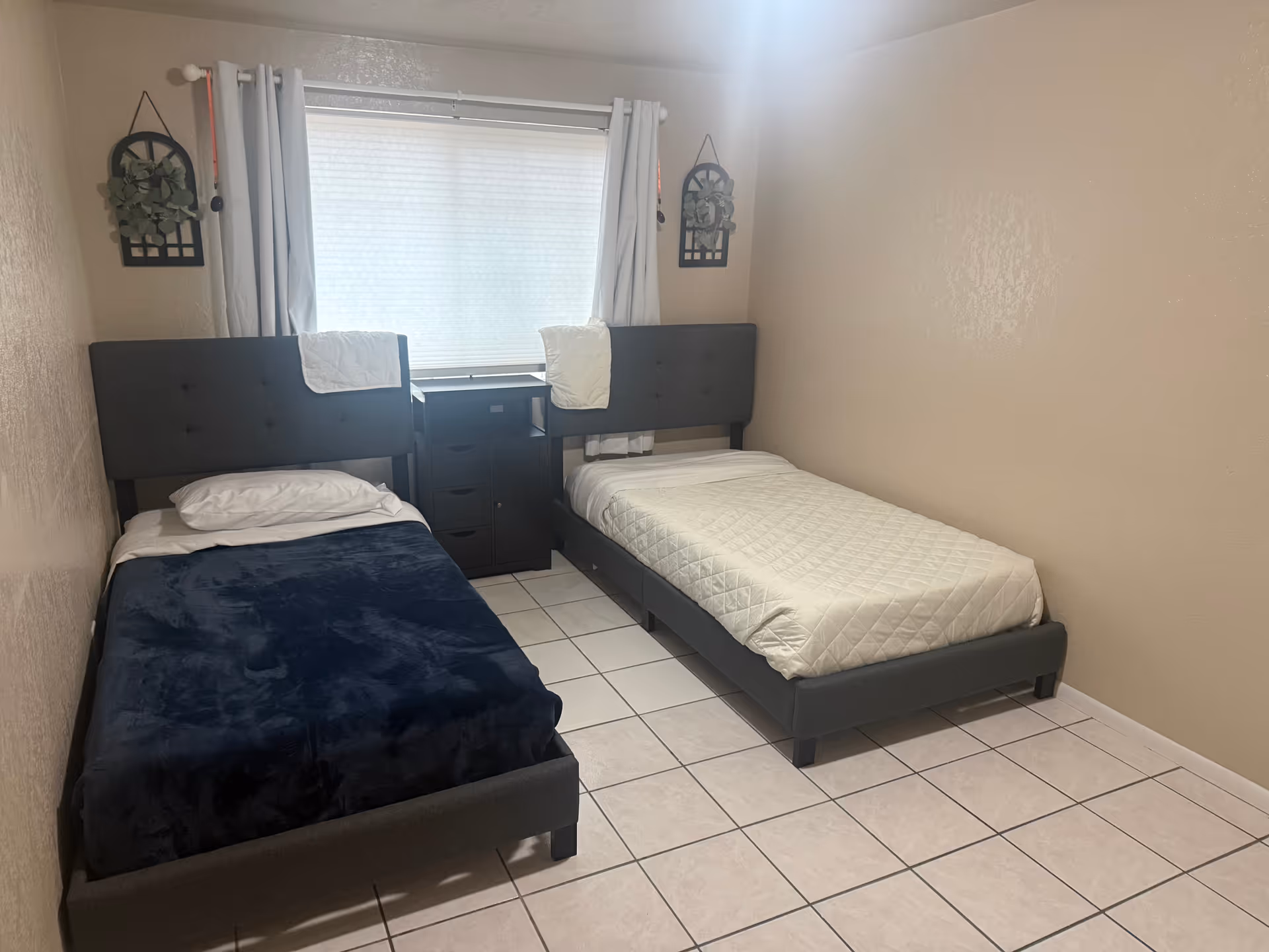 Two twin beds with dark headboards, a nightstand, window, and tiled floor.