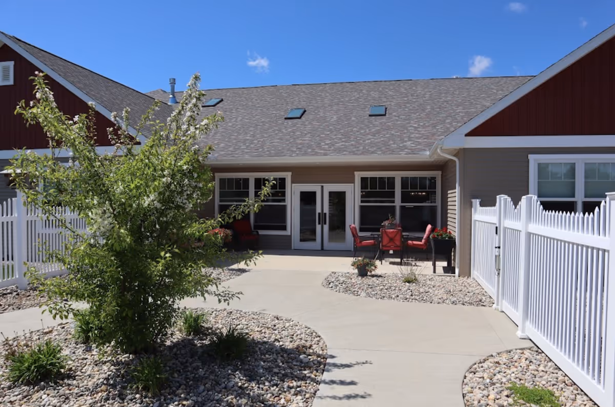 Exterior of The Laurels of Goshen with a fenced patio and red chairs.