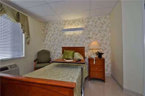 Single bedroom with a wooden bed, dresser, chair, and floral wallpaper.