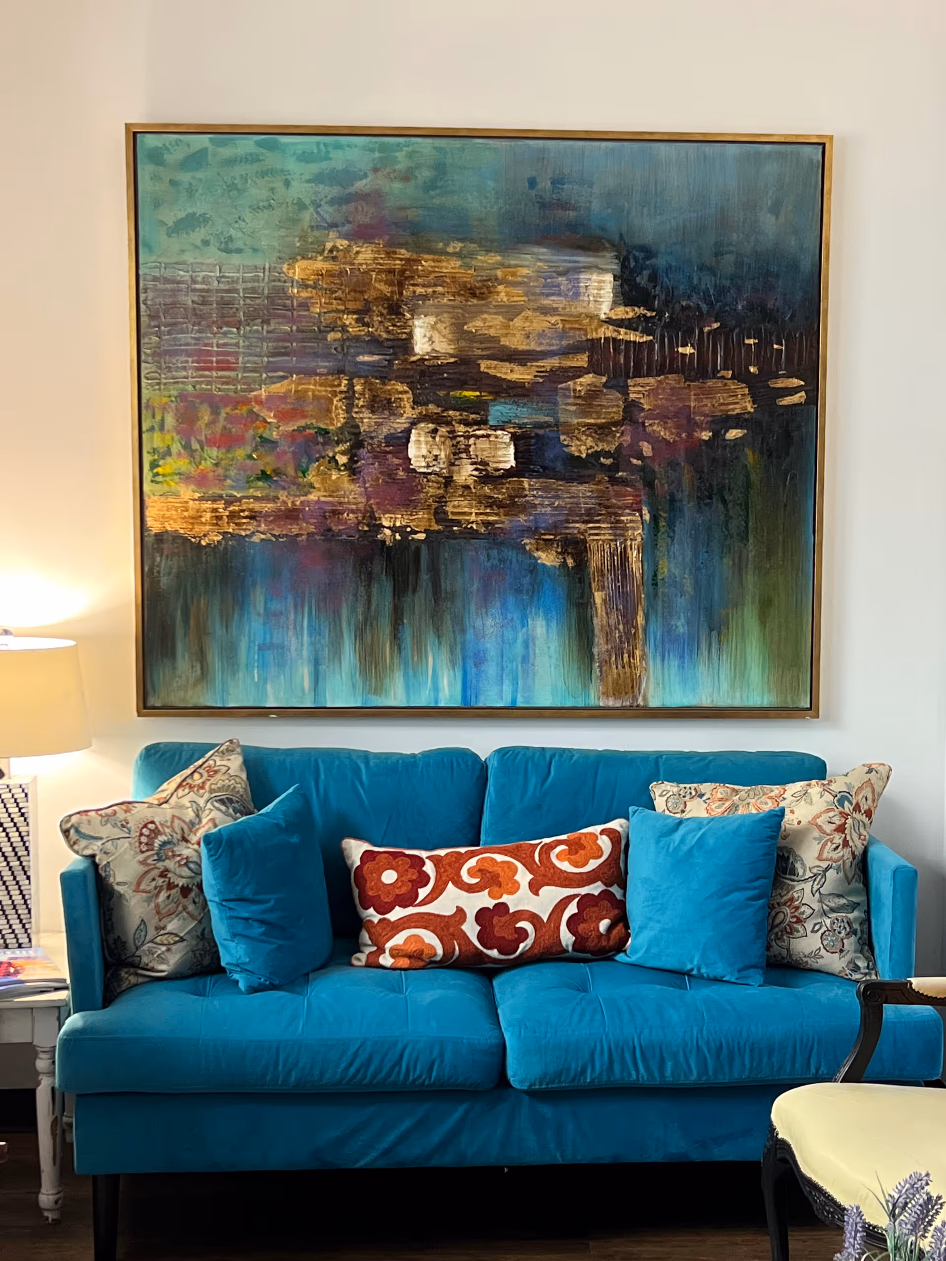 Bright blue sofa with patterned cushions sits under a large abstract painting in a living room.