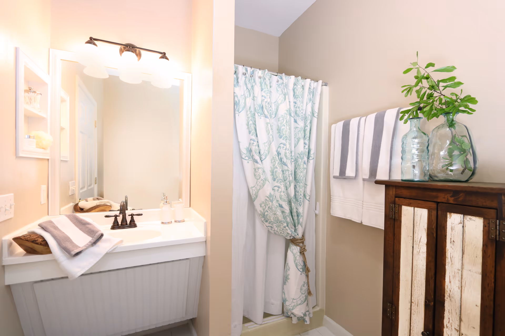 Bright bathroom with sink, mirror, towels, shower curtain, and wooden cabinet.