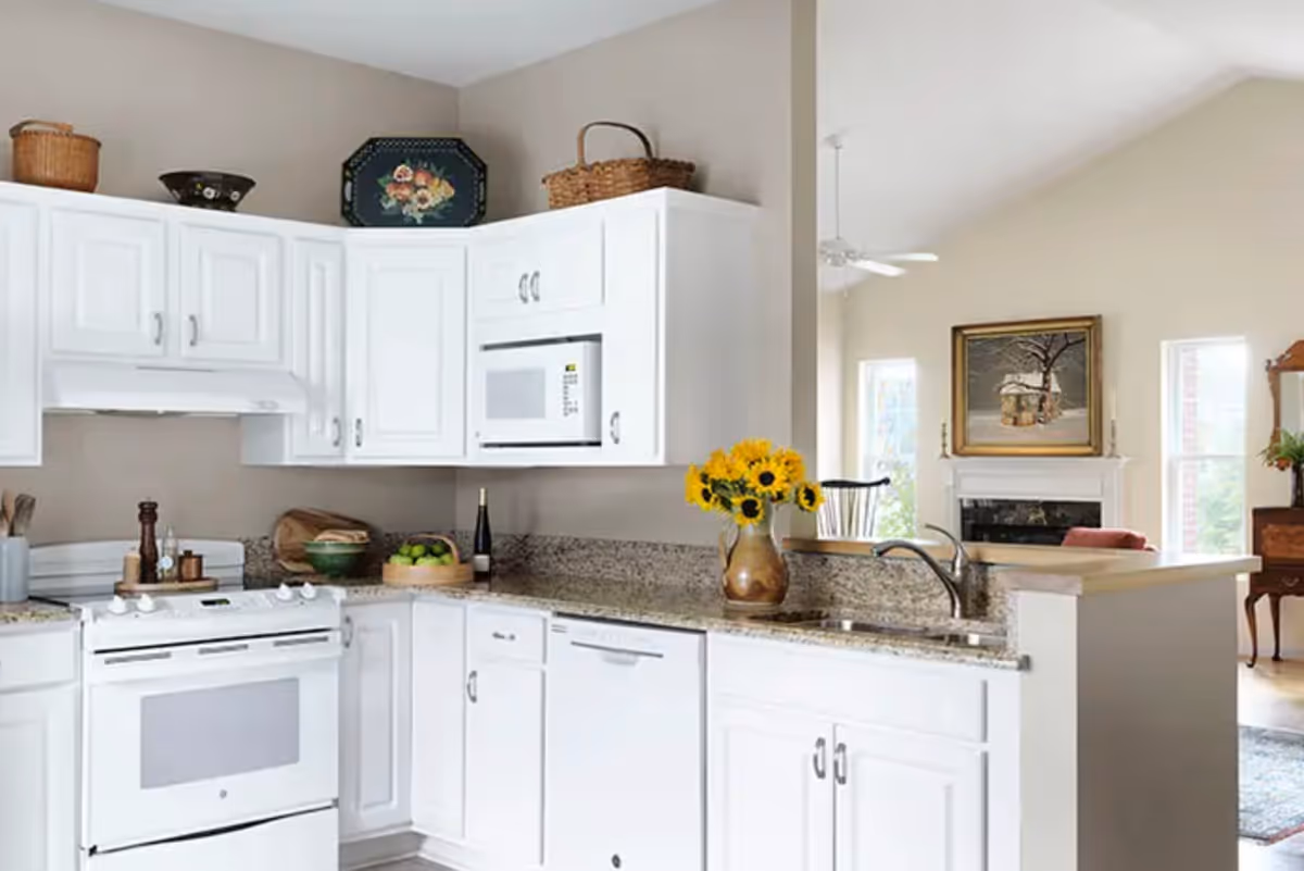 Bright white kitchen with granite countertops and sunflowers, open living area visible beyond.