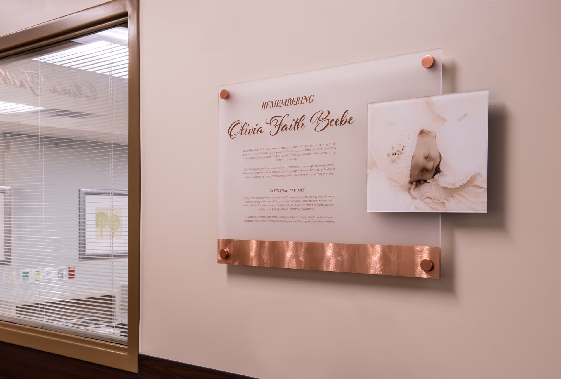 Memorial plaque on wall with baby photo in a beige hallway inside Drew Memorial Health System.