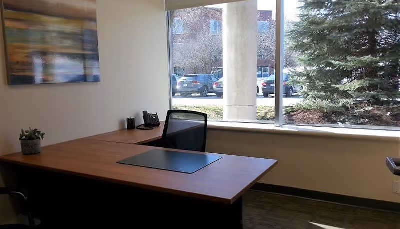 Office desk and chair by a large window overlooking a parking lot.