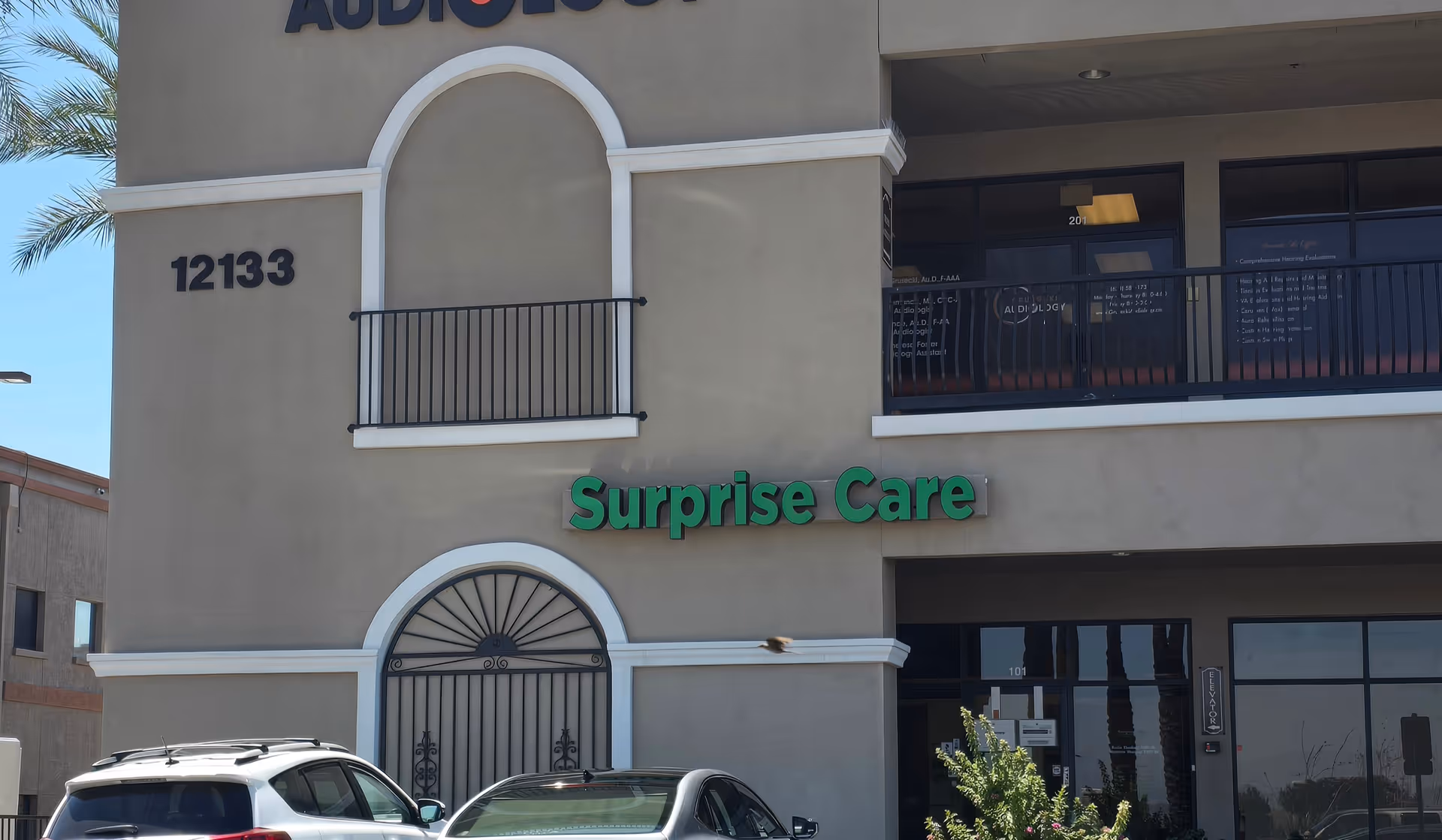 Facade of Surprise Care facility with green sign, balconies, and parked cars in front.