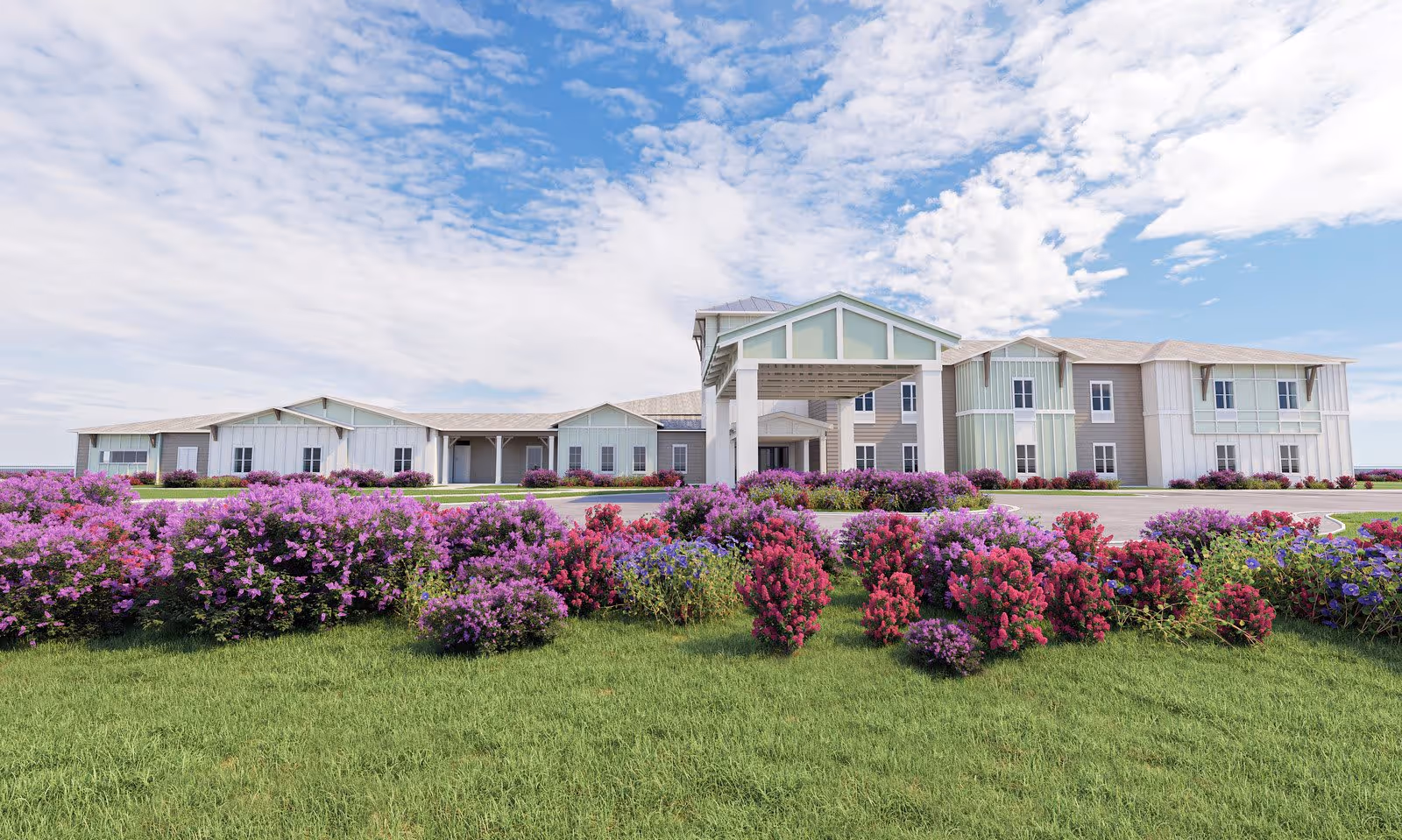 Exterior view of The Canopy at Boynton Ridge facility with a large, modern building featuring multiple windows and a covered entrance. The foreground has a well-maintained lawn and vibrant flower beds with purple and pink flowers under a partly cloudy blue sky.