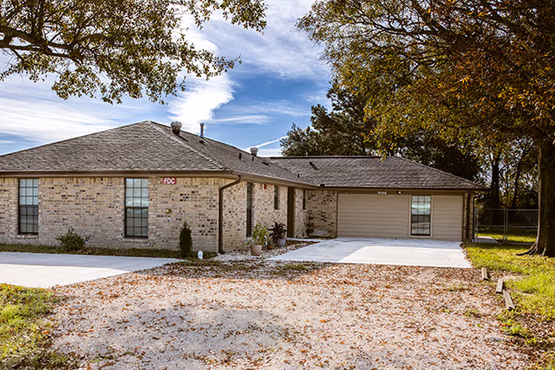 Single-story brick senior living facility with driveway, garage, and trees.