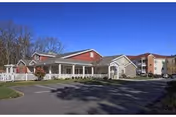 Front view of ThriveCare Assisted Living building with red roof and white porch, parking lot.