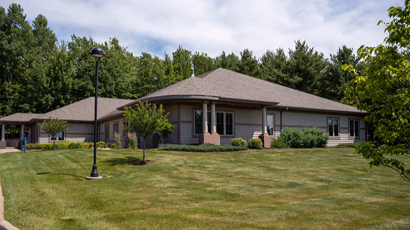 Single-story building with a manicured lawn, trees, and a covered entrance.