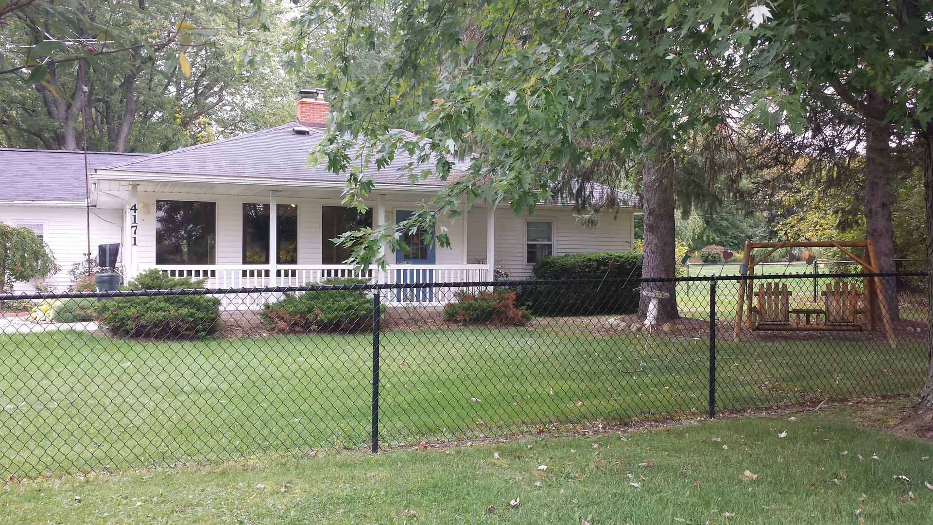 Front view of a single-story senior living facility with porch and chain-link fence.