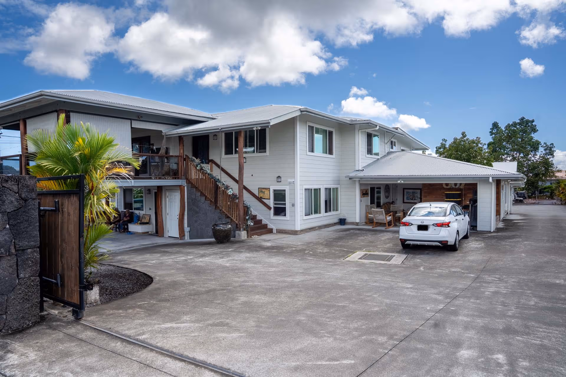 Two-story light-gray senior living building with a driveway, stairs, and a parked white car.