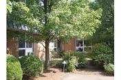 Brick senior living facility exterior with windows, trees, and landscaped shrubs.
