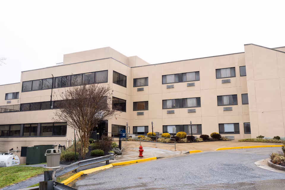 Exterior view of a beige multi-story senior living facility with driveway and landscaping.