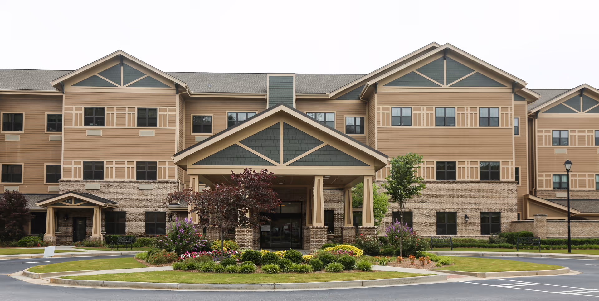 Front exterior view of Chelsey Park Health & Rehabilitation building with a covered entrance, landscaped garden with flowers and shrubs, and a circular driveway.