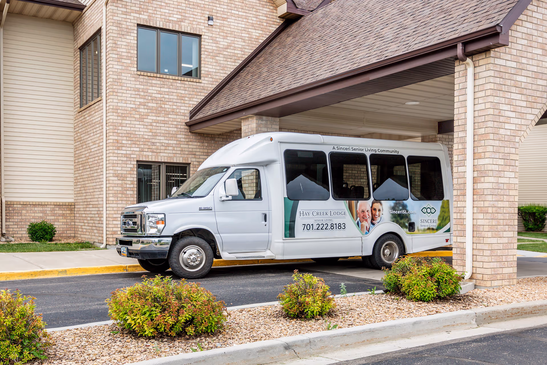 A white shuttle van parked outside a brick senior living facility entrance.