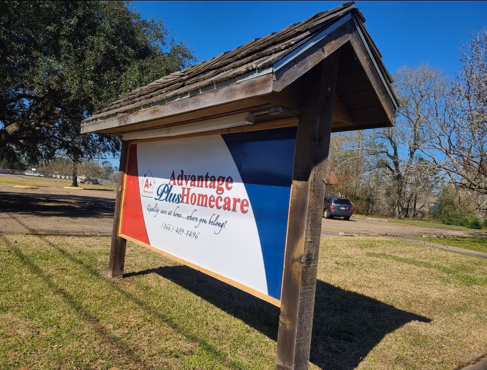 Outdoor signboard for Advantage Plus Homecare under a wooden shelter in a grassy area.