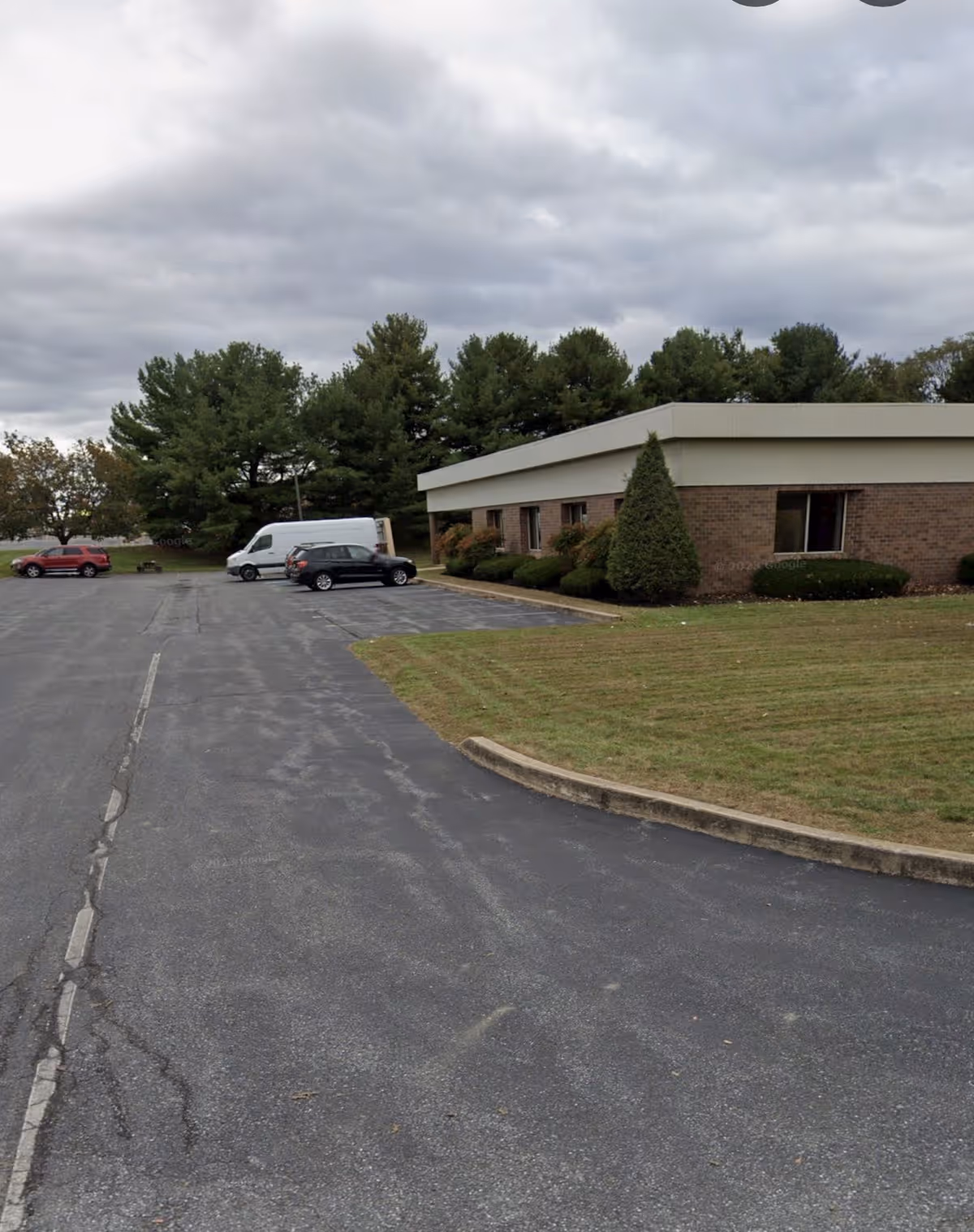 Exterior view of a brick senior living facility with a parking lot and trees.