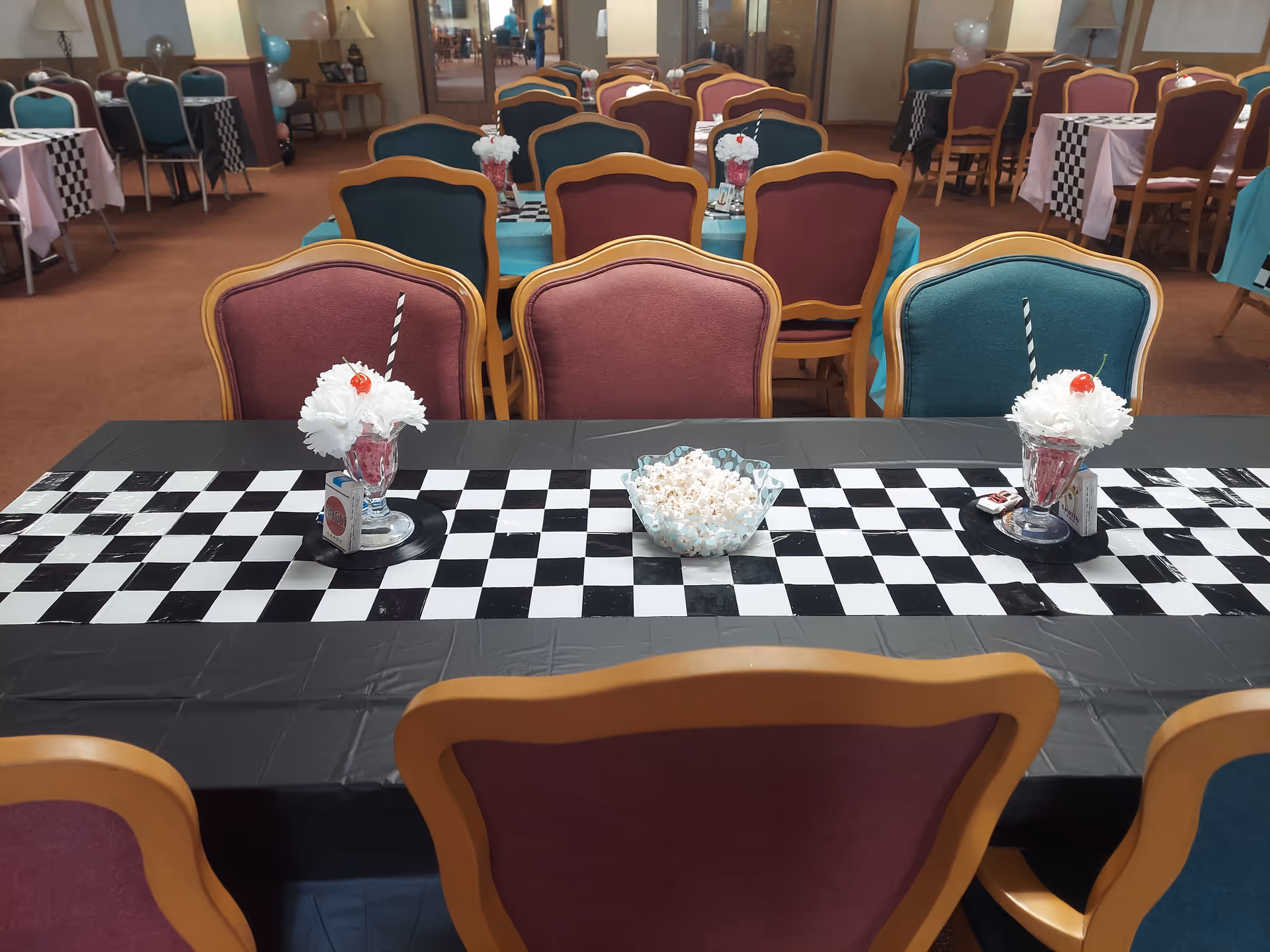 Senior living dining room with checkered table runner, colorful chairs, and popcorn centerpiece.