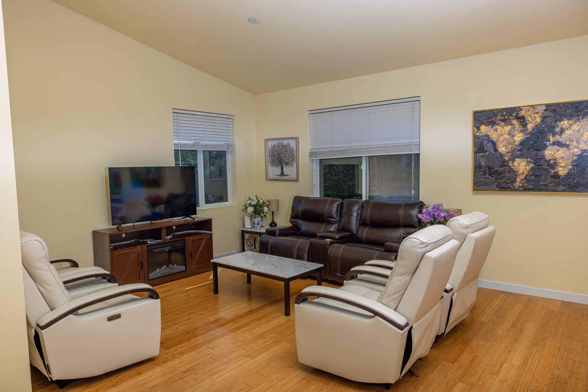 Cozy living room with cream recliners, a leather sofa, TV, coffee table, and artwork.