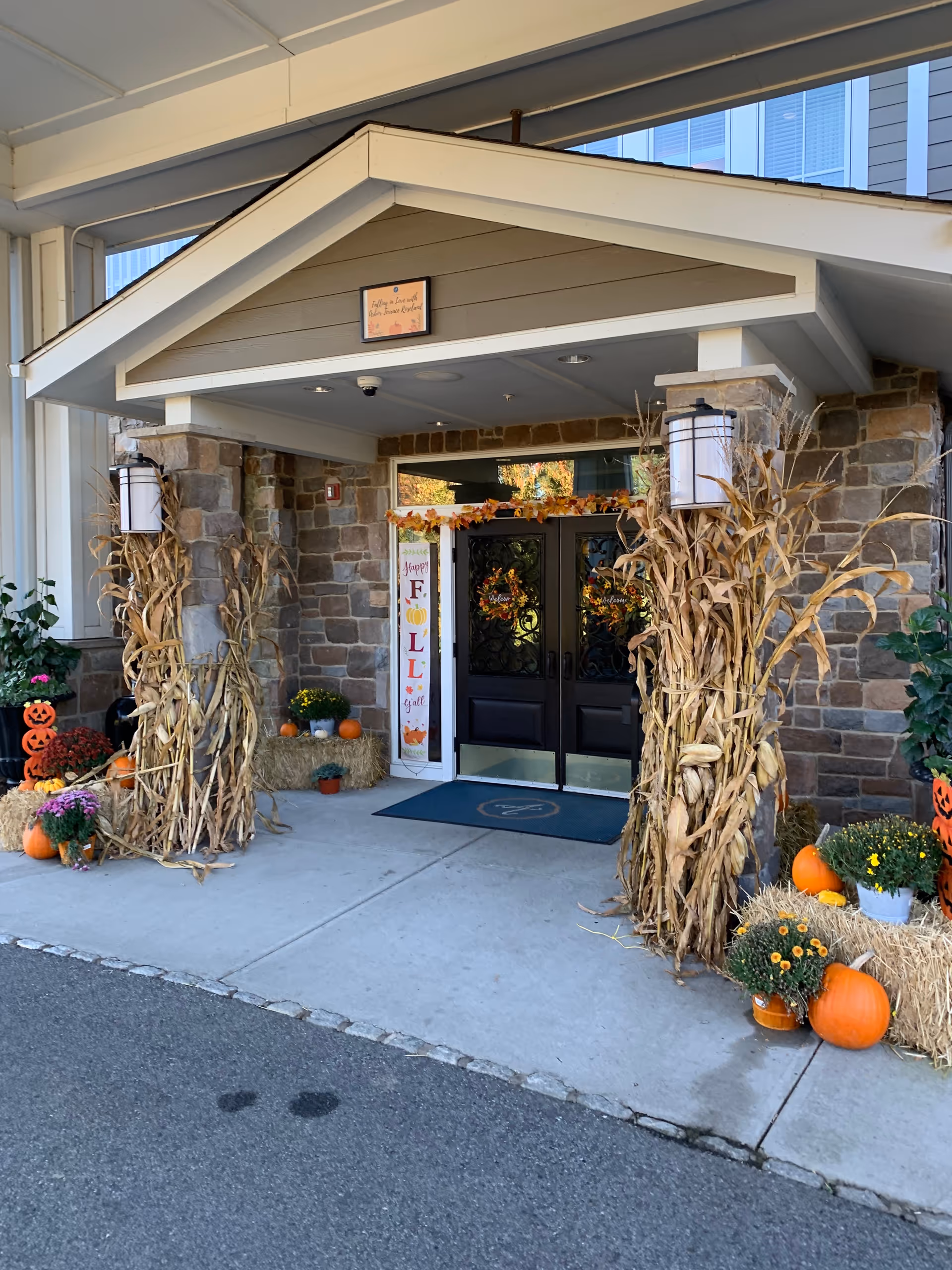 Stone entrance with fall decor, corn stalks, pumpkins, and wreaths at Arbor Terrace Roseland.